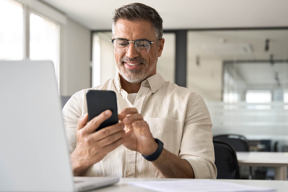 Homem mexendo em celular vendo os benefícios do software de cobranças