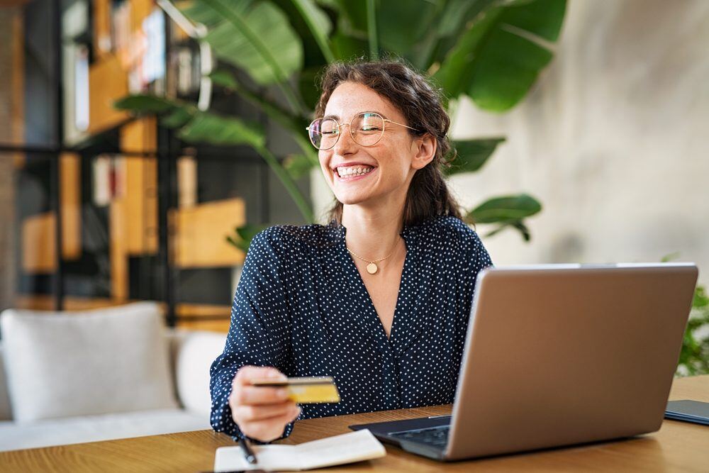 Mulher sorrindo com cartão de crédito na mão e um notebook