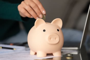 Homem colocando moedas em um cofre com formato de um porco de porcelanato