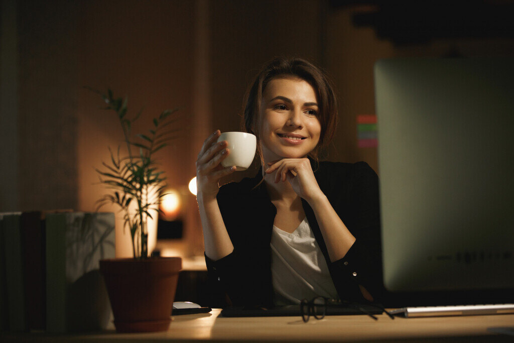 mulher com xícara na mao sorrindo com os braços apoiados em uma mesa