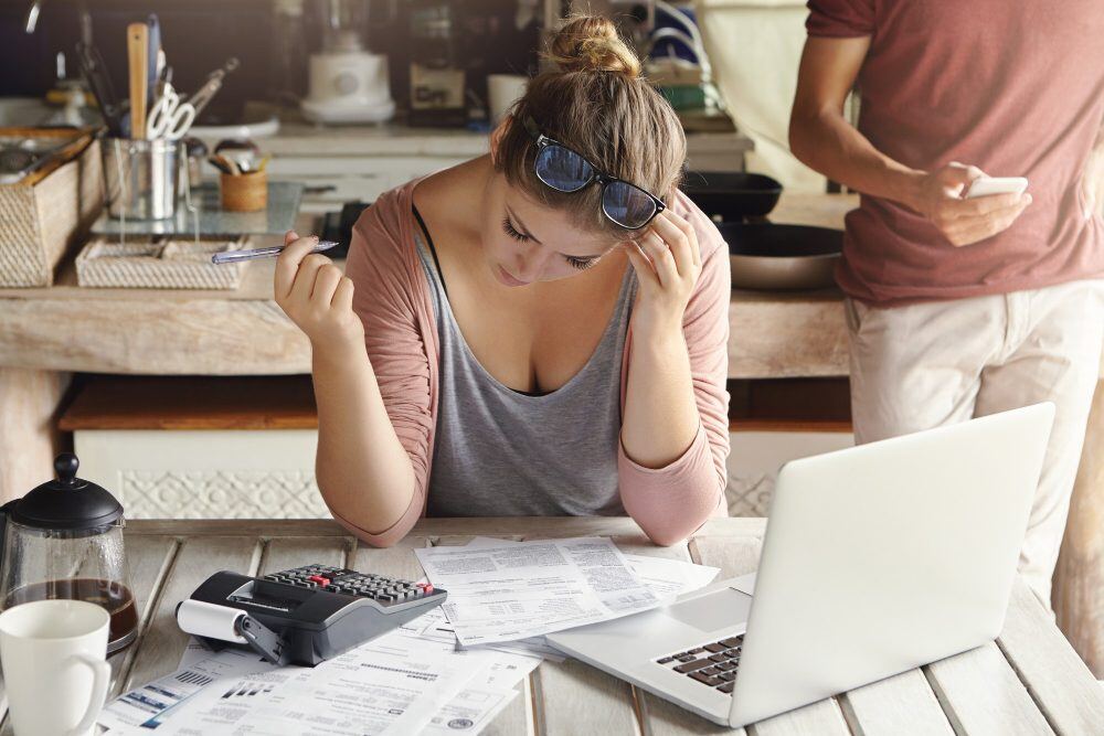 Mulher com mãos na cabeça, contas calculadora e notebook na frente em cima de mesa