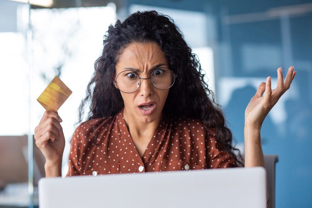 Mulher com cartão de crédito e com cara preocupada olhando para Notebook